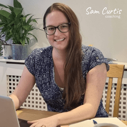 Sam Curtis Coaching: Sam sat at desk smiling with plants in the background